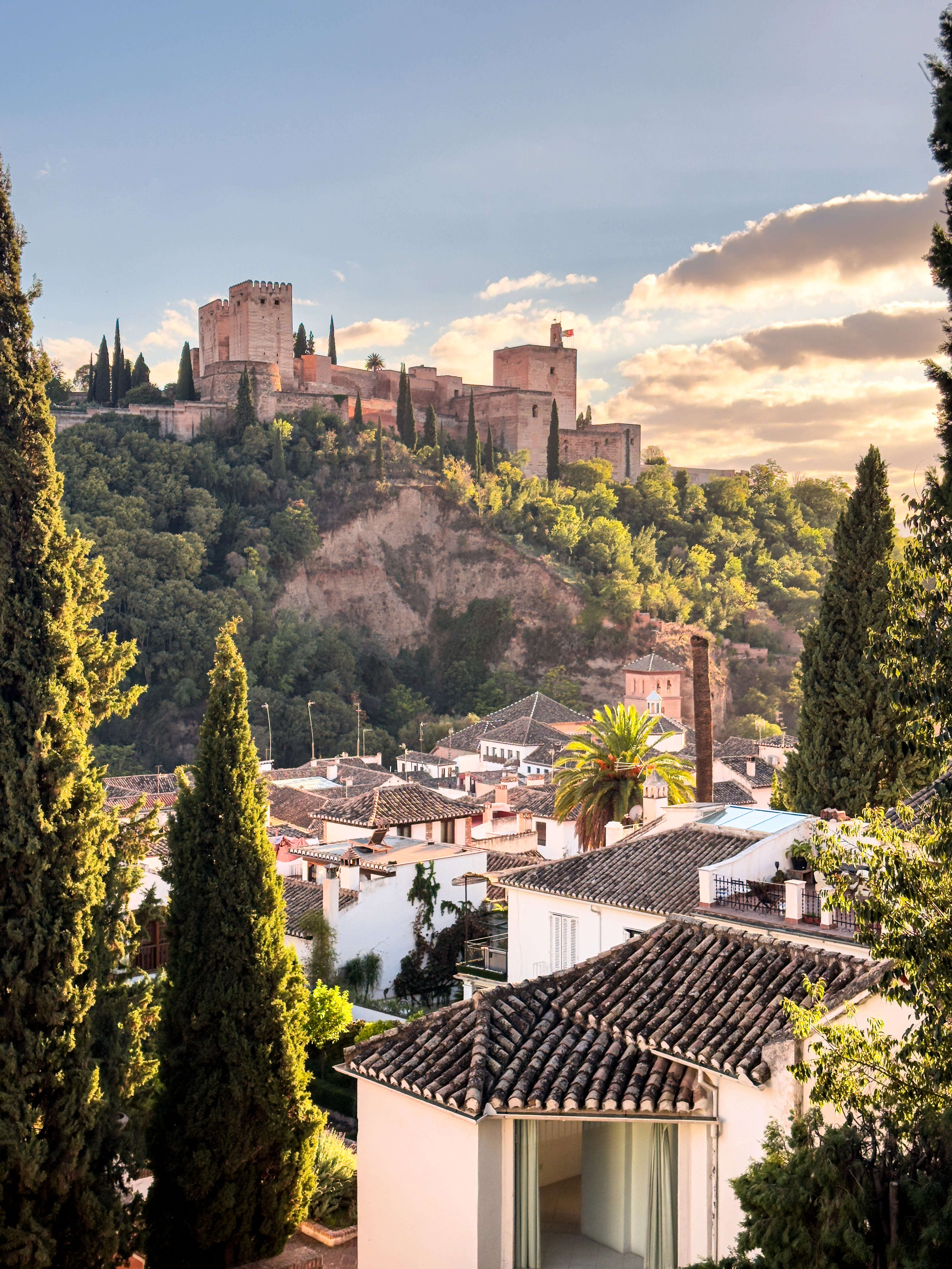 Granada hillside with cypress trees, white buildings, and fortress walls.