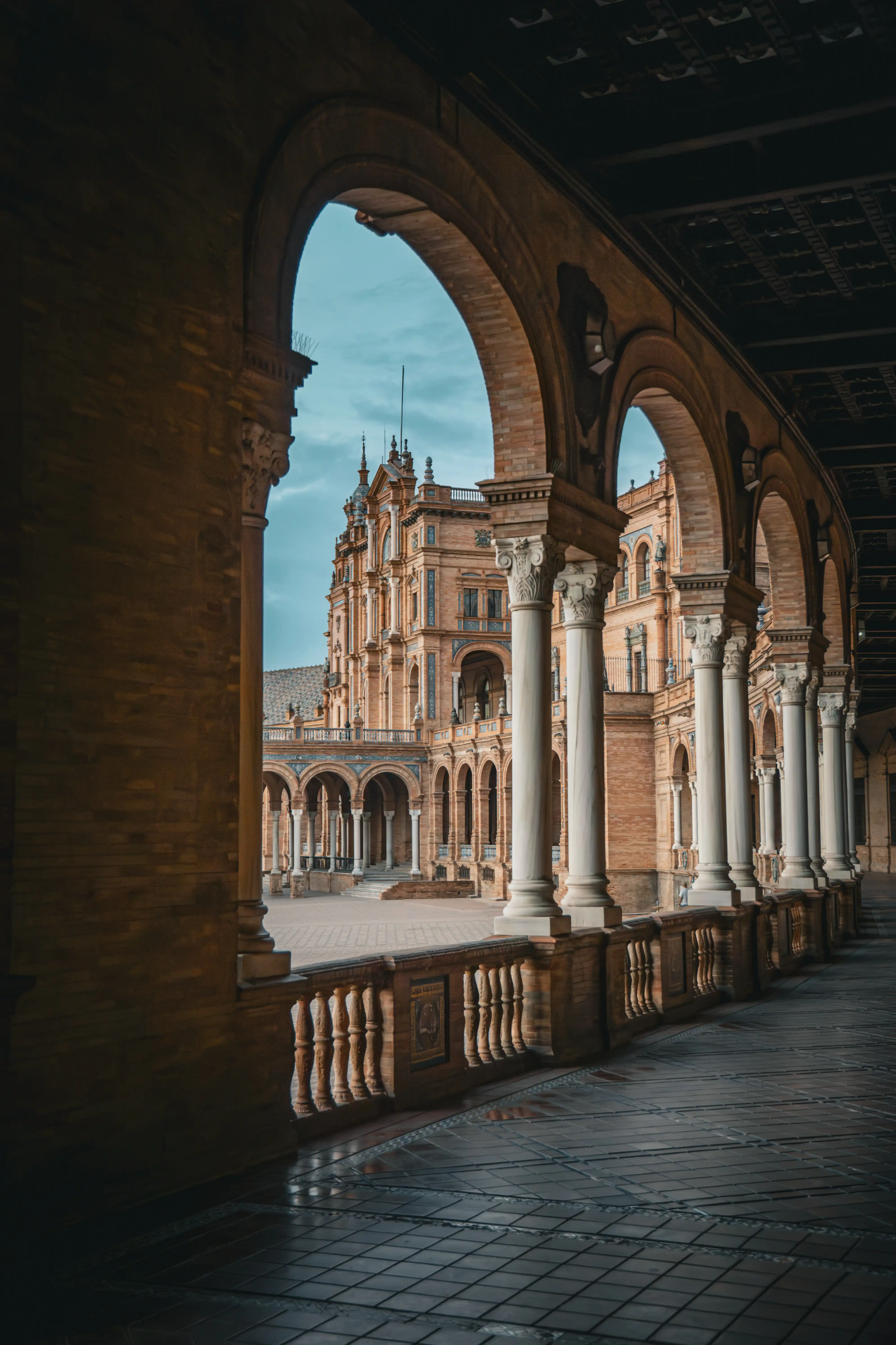 View through shaded arches toward an ornate Spanish plaza.