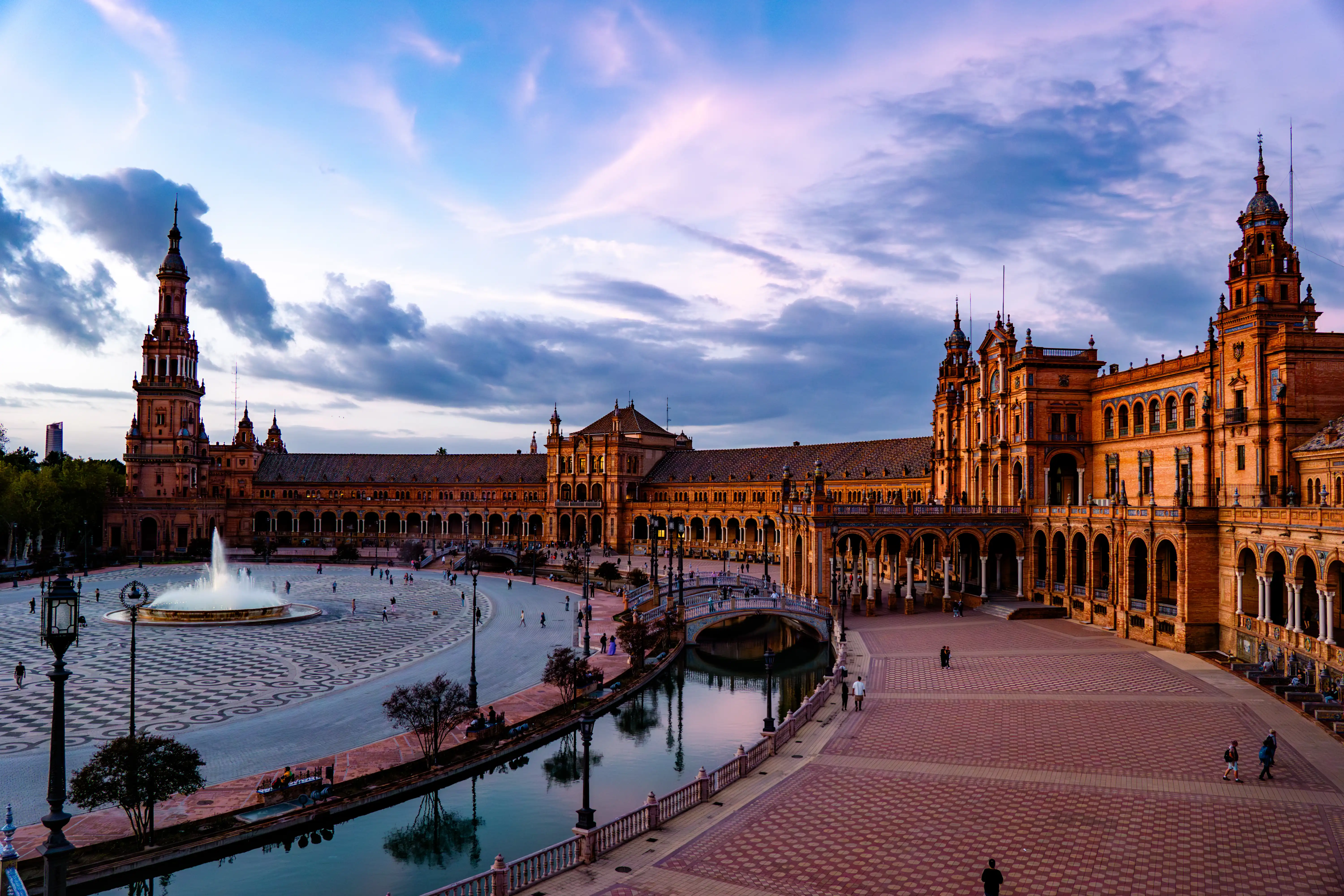 Wide Spanish plaza with ornate buildings and soft evening clouds.