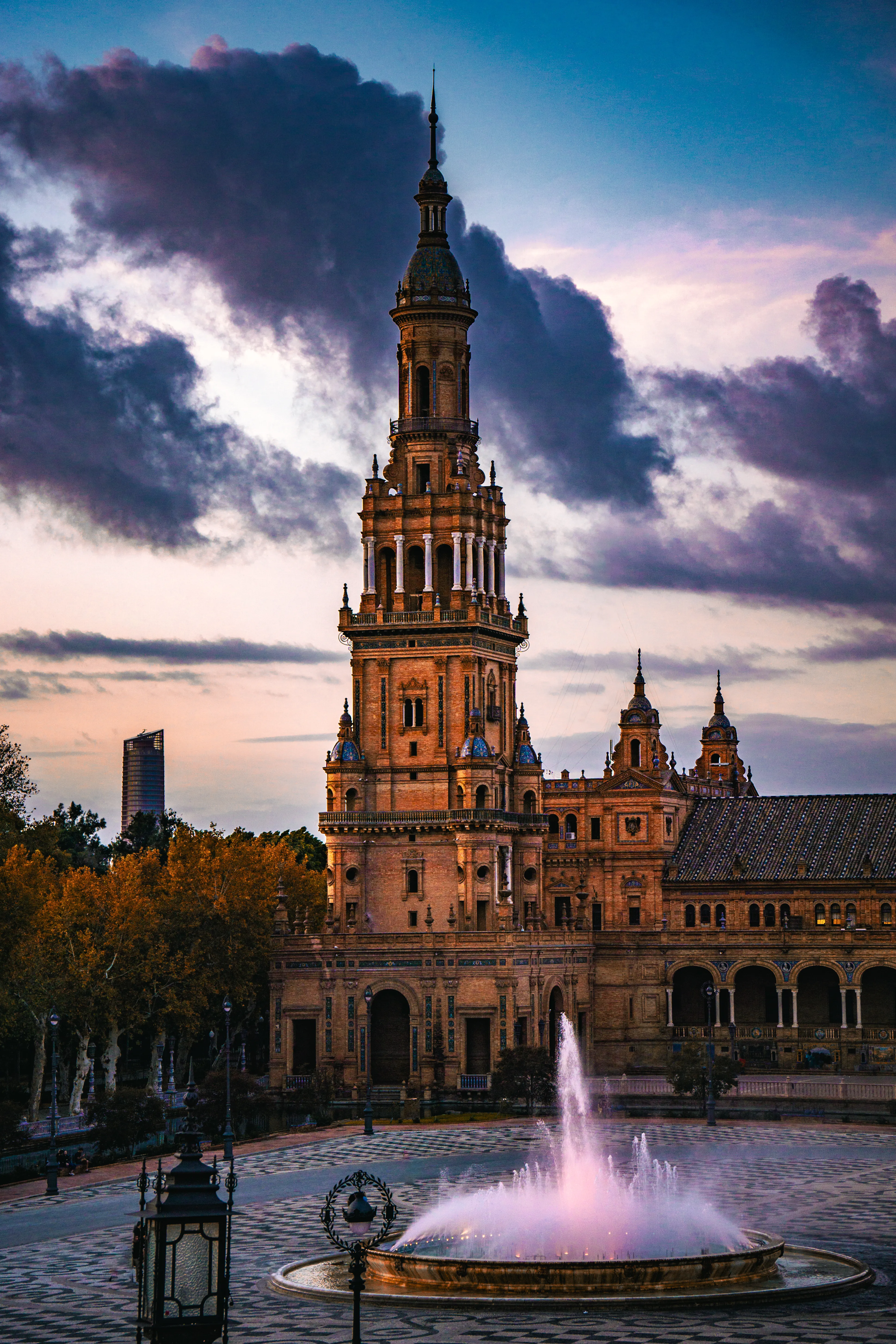 Spanish tower and fountain under dramatic evening clouds.
