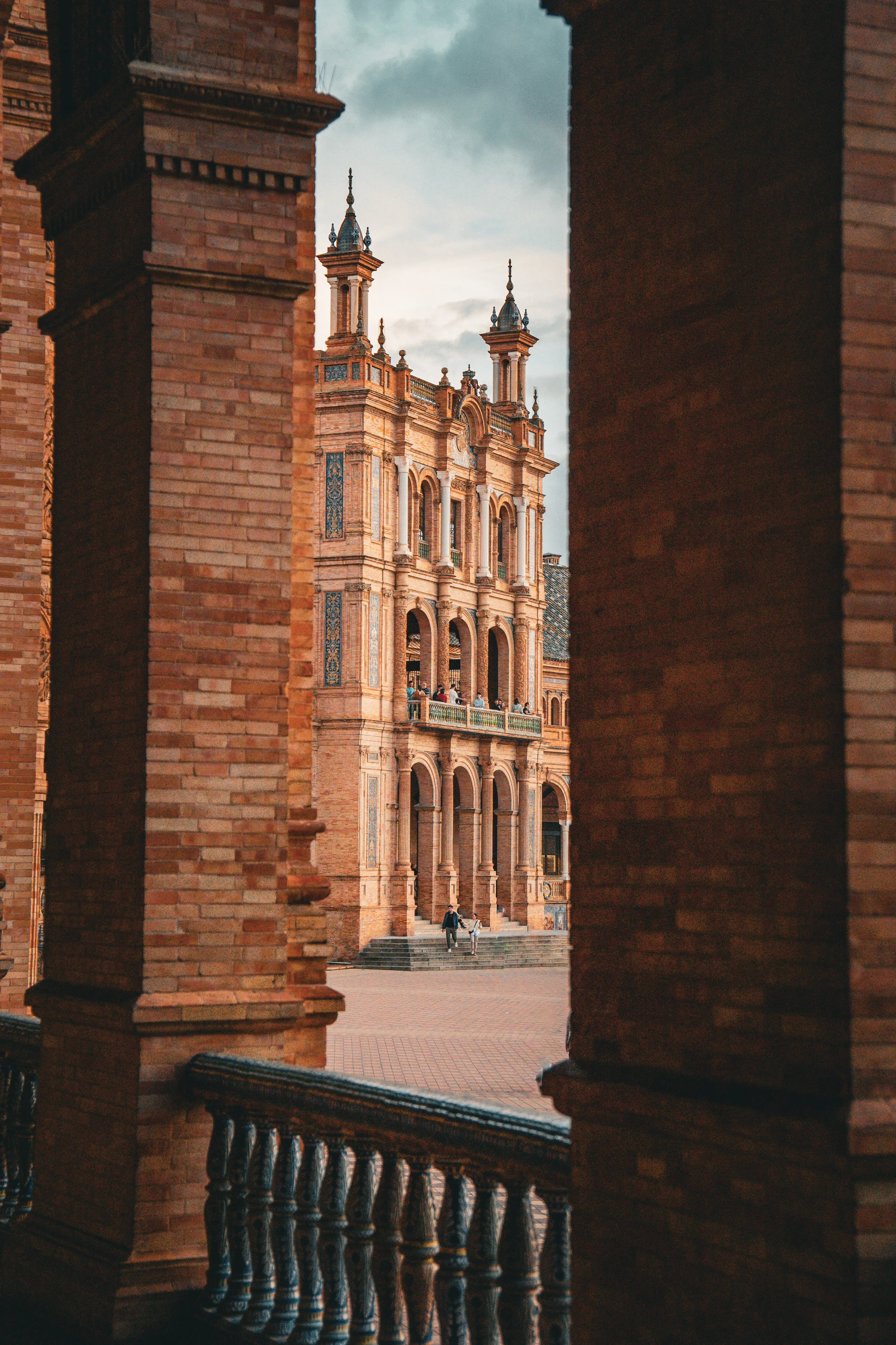 View of an ornate Spanish plaza through dark brick columns.
