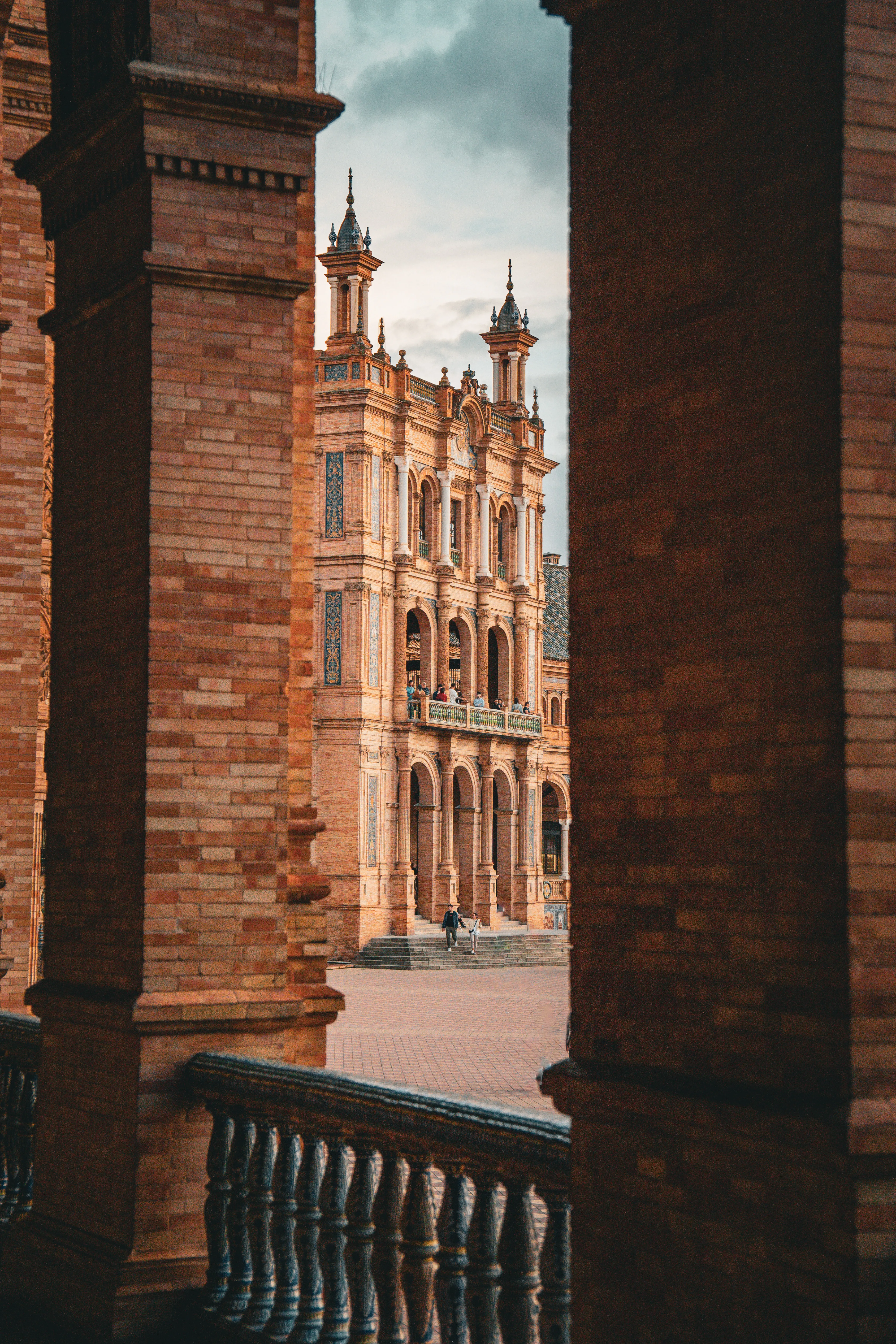 View of an ornate Spanish plaza through dark brick columns.