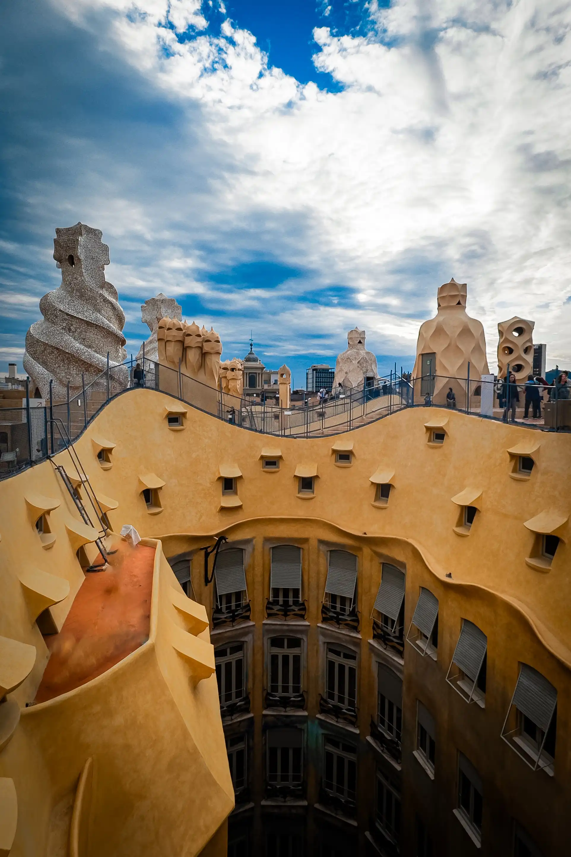 Curved yellow facade and roof details of Casa Batllo under blue sky.