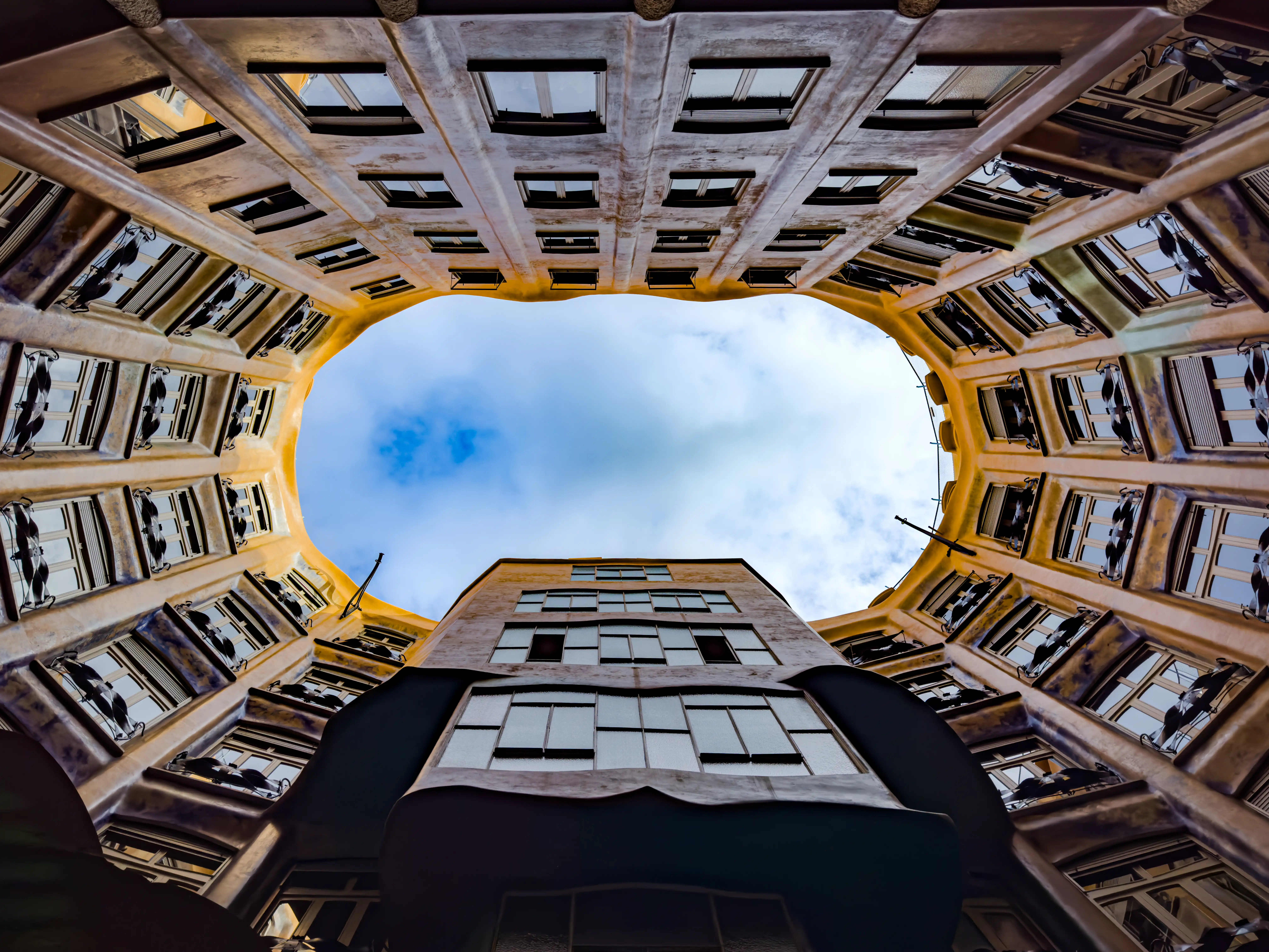 Looking up through a square courtyard toward blue sky and surrounding balconies.