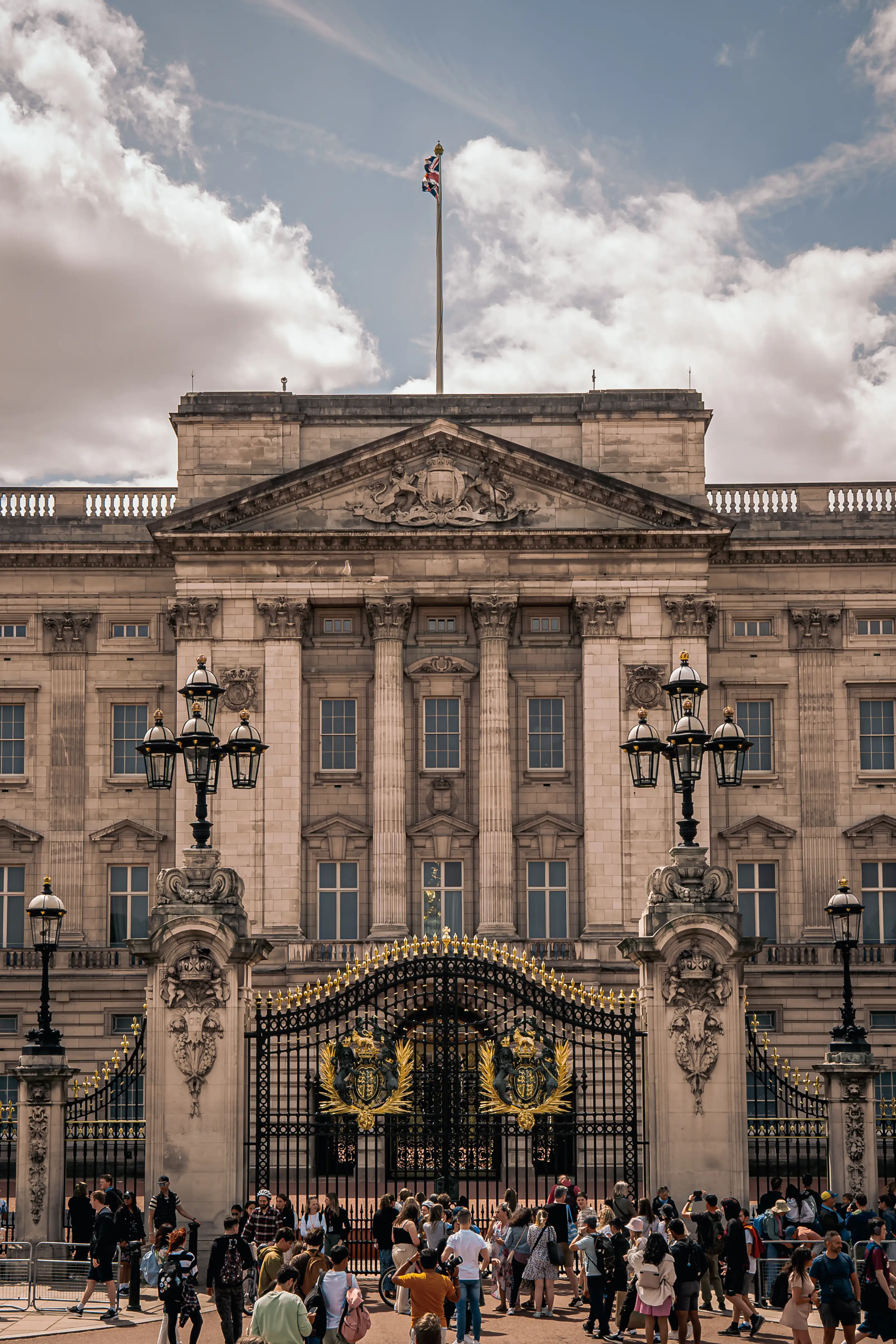 Buckingham Palace facade and gates with people gathered outside.
