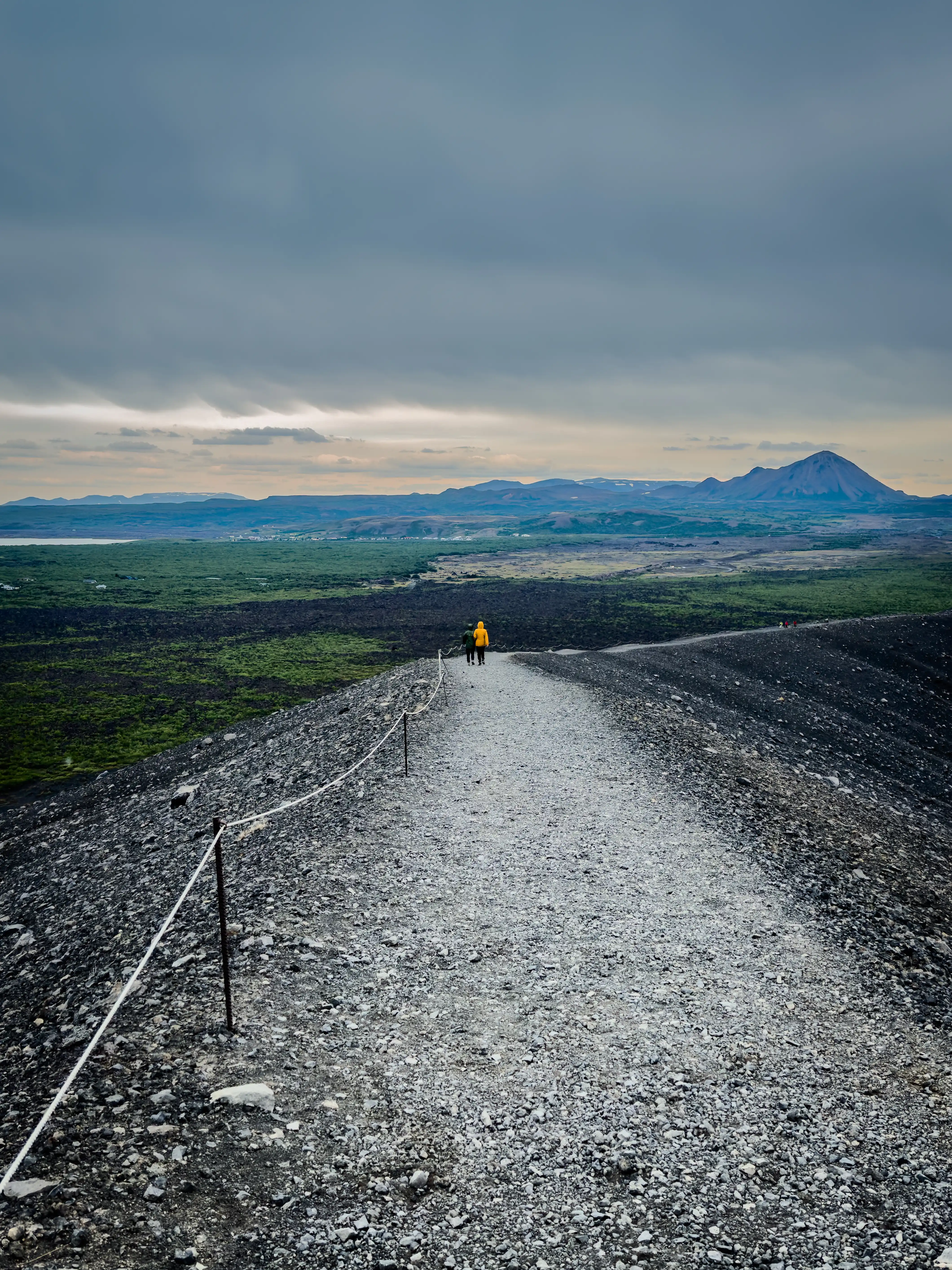 Person walking along a gravel road toward distant Icelandic mountains.