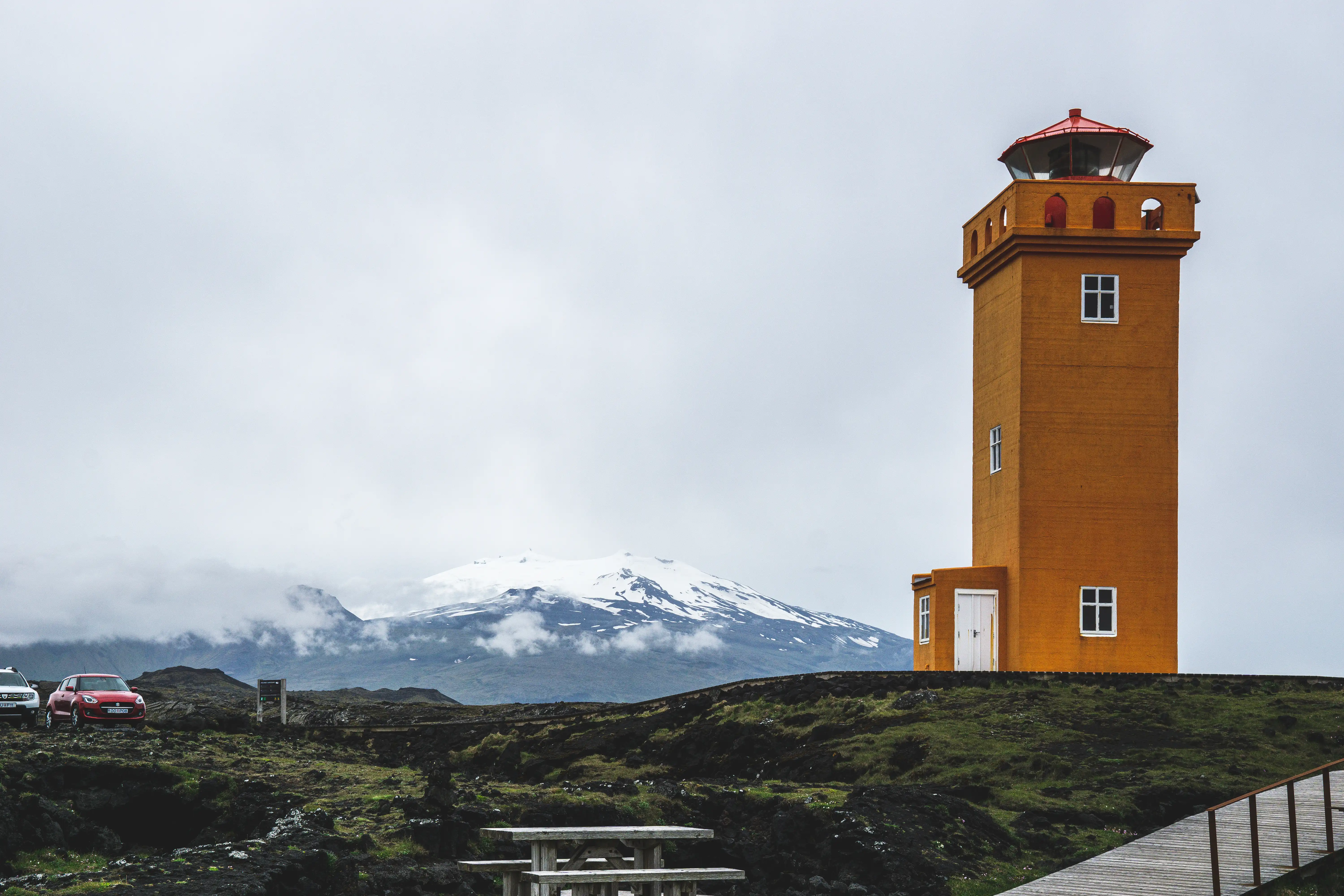 Orange lighthouse in Iceland with mountains and clouds behind it.