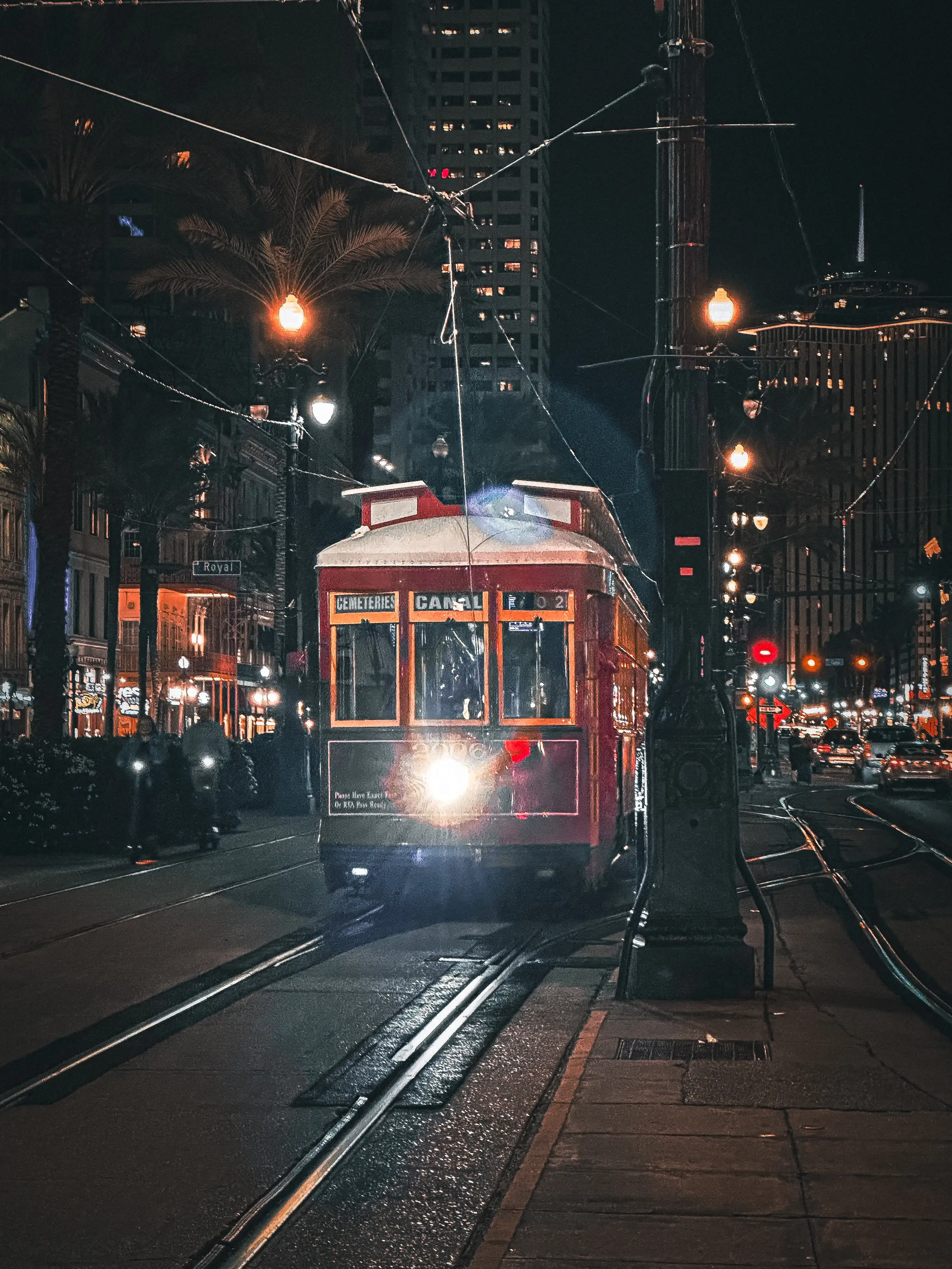 Red tram approaching at night on a rainy city street.