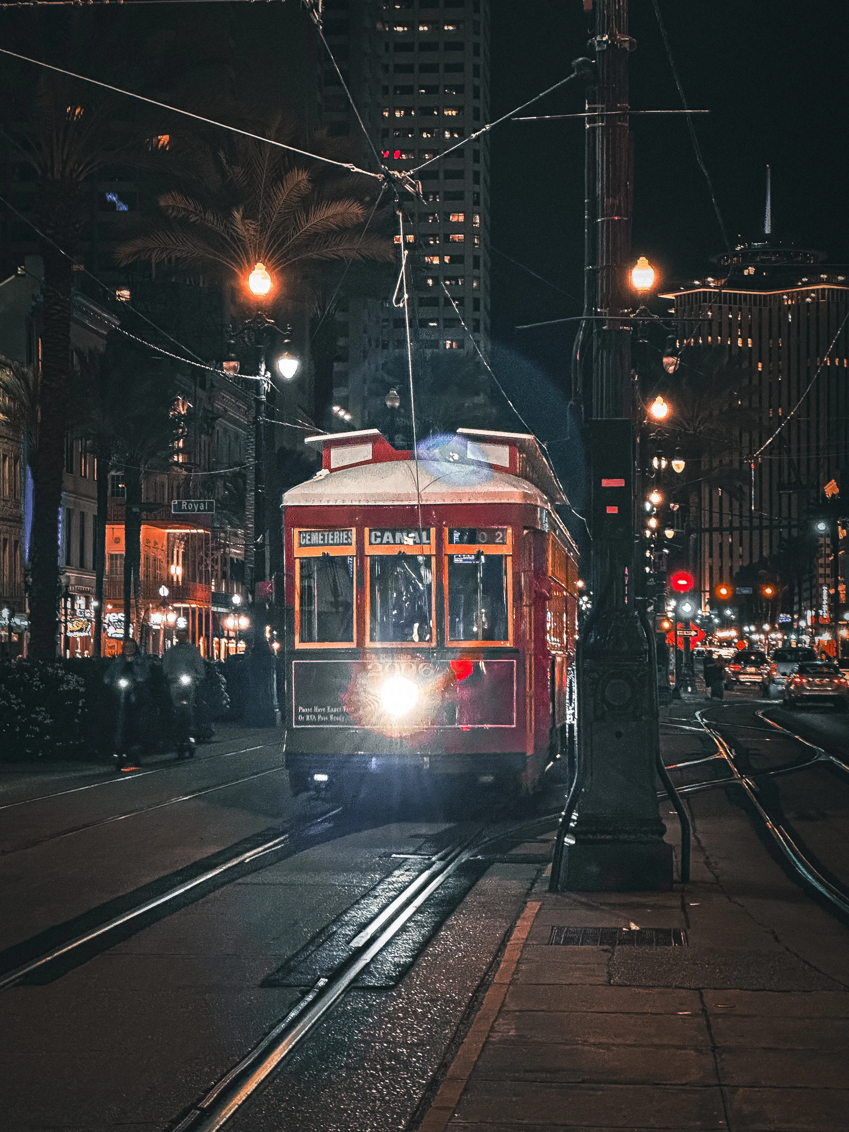 Red tram approaching at night on a rainy city street.