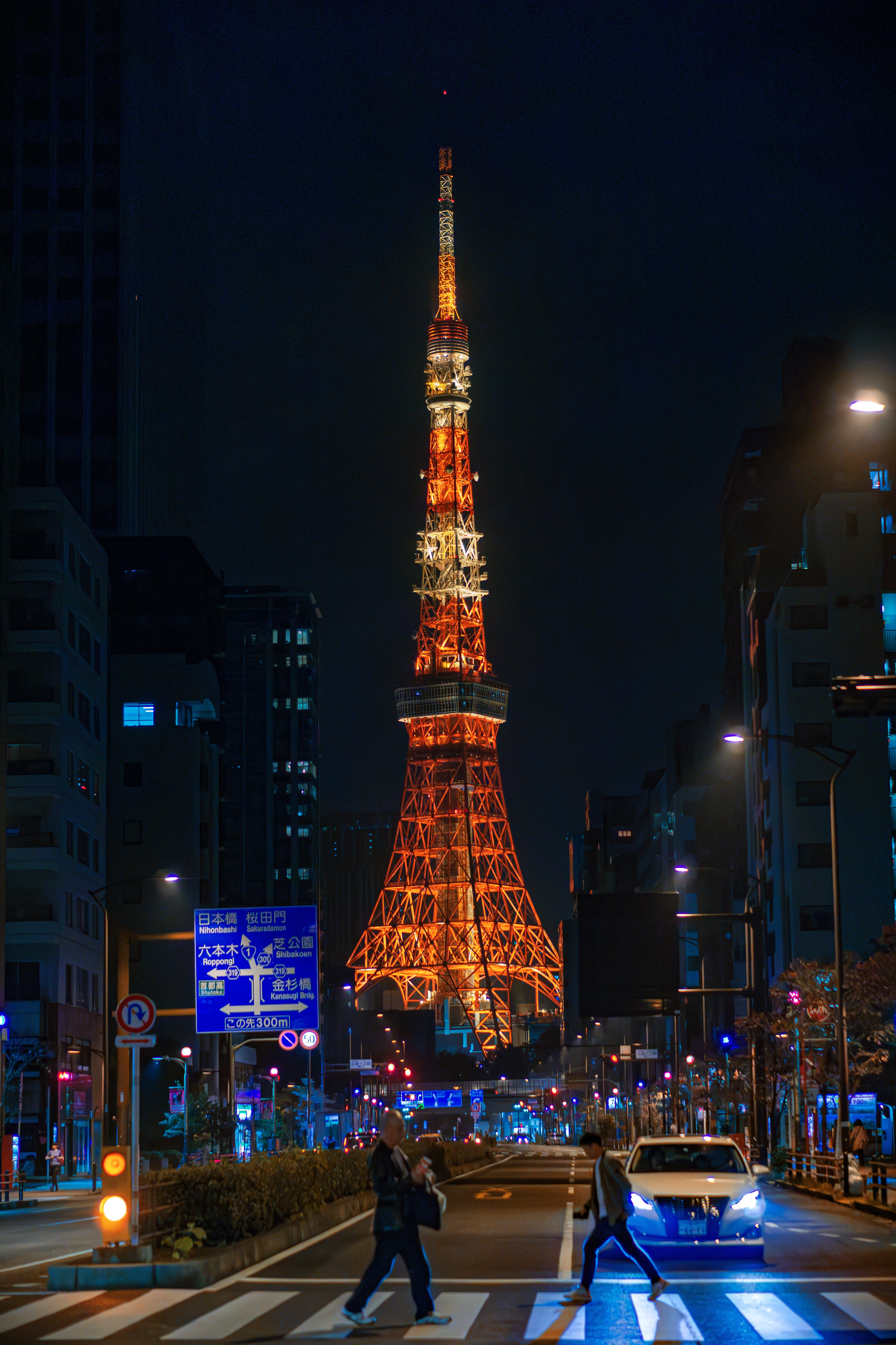 Tokyo Tower glowing orange above a nighttime city street.