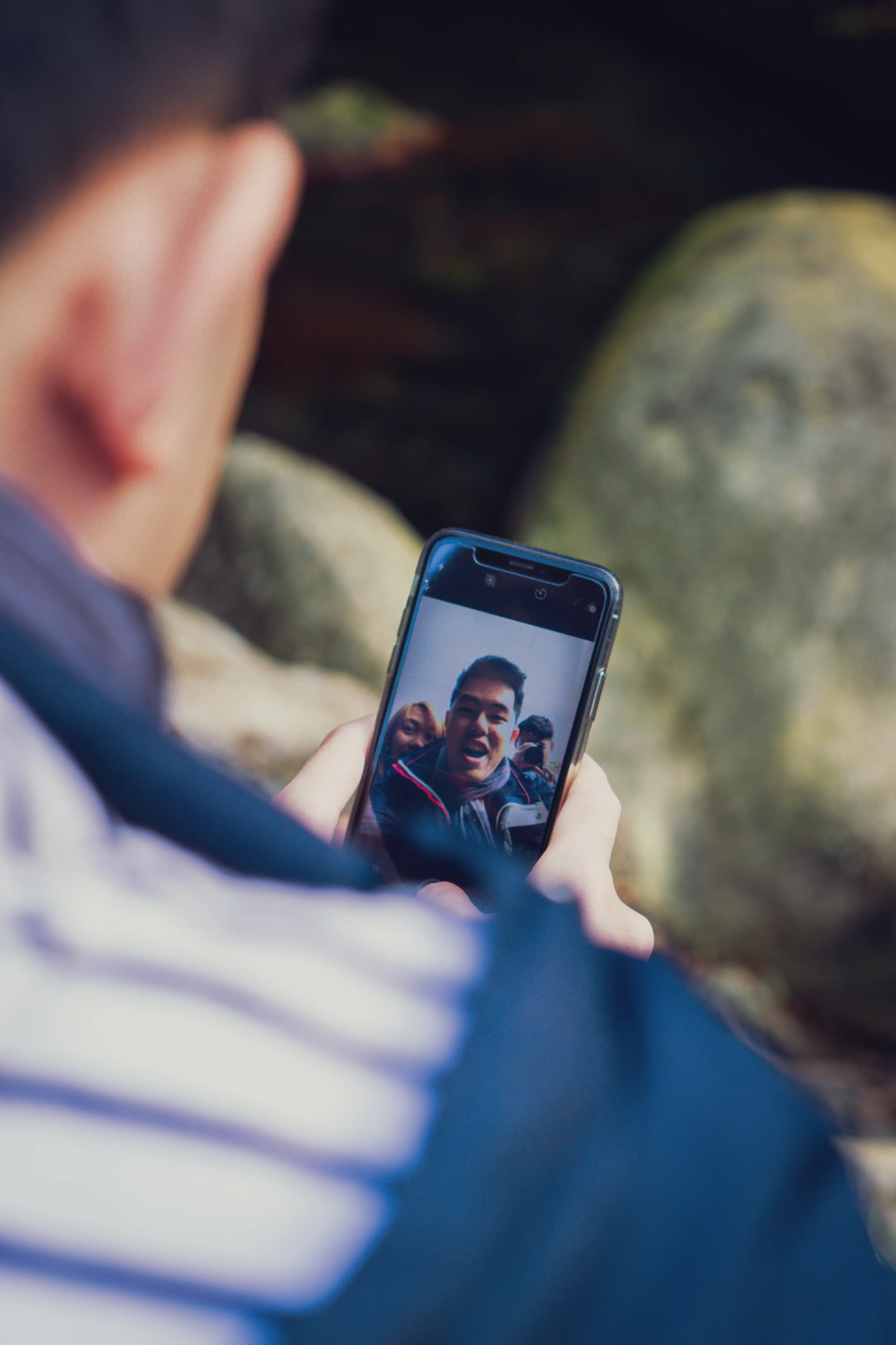Person holding a phone showing a photo while seated outdoors.