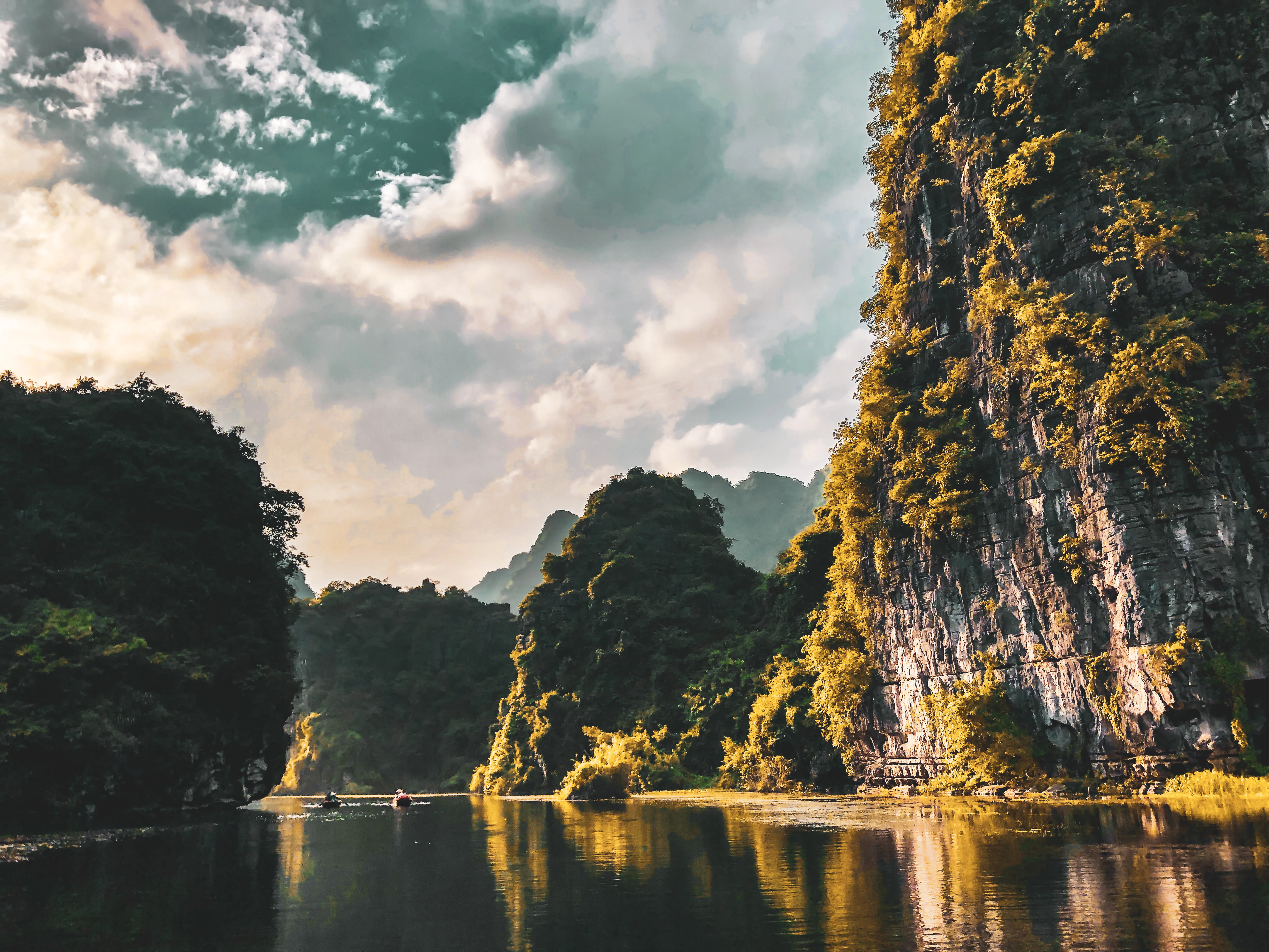 Limestone cliffs reflected in calm water beneath a bright cloudy sky.
