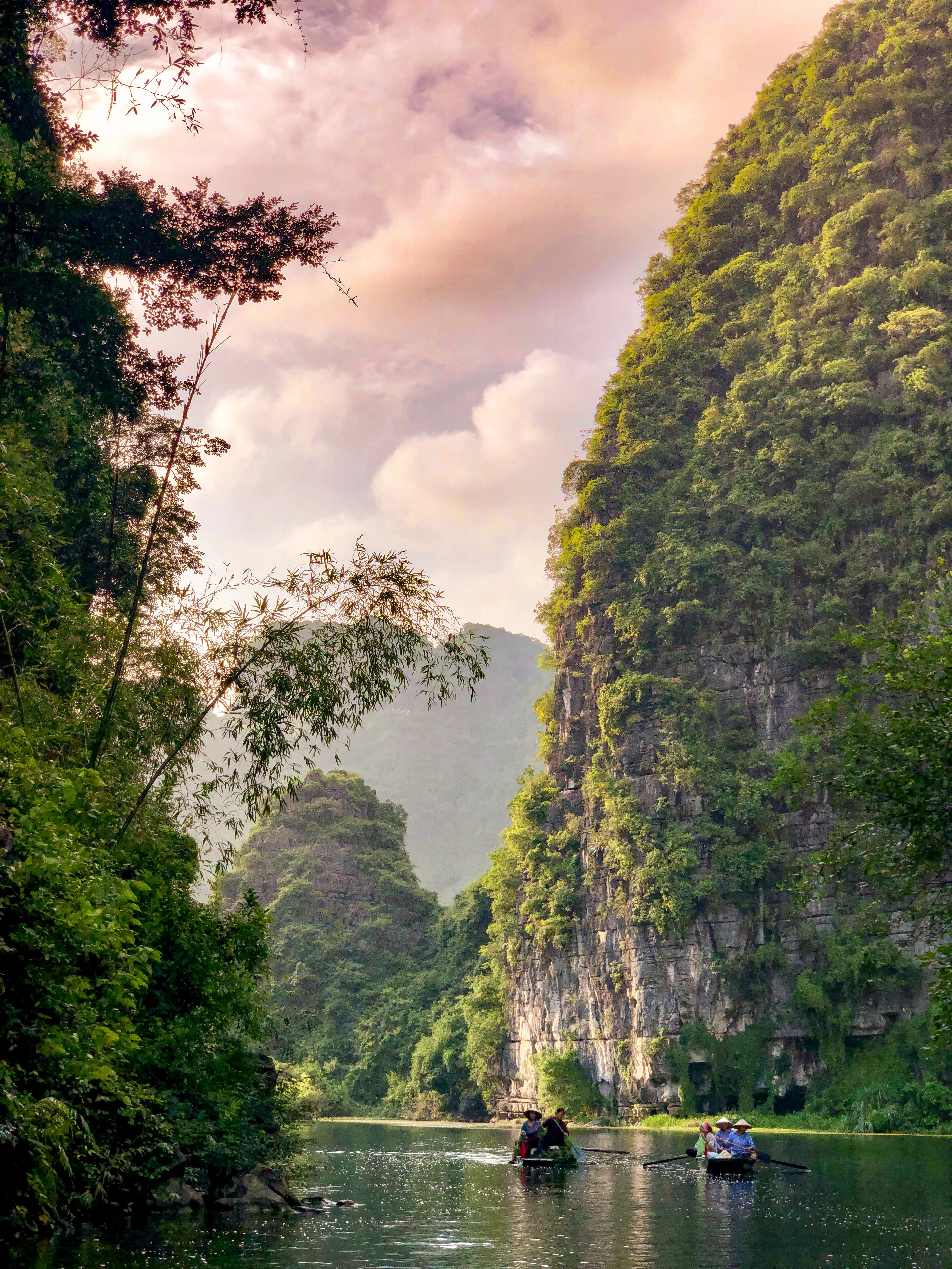 Small boats traveling between steep green limestone cliffs.