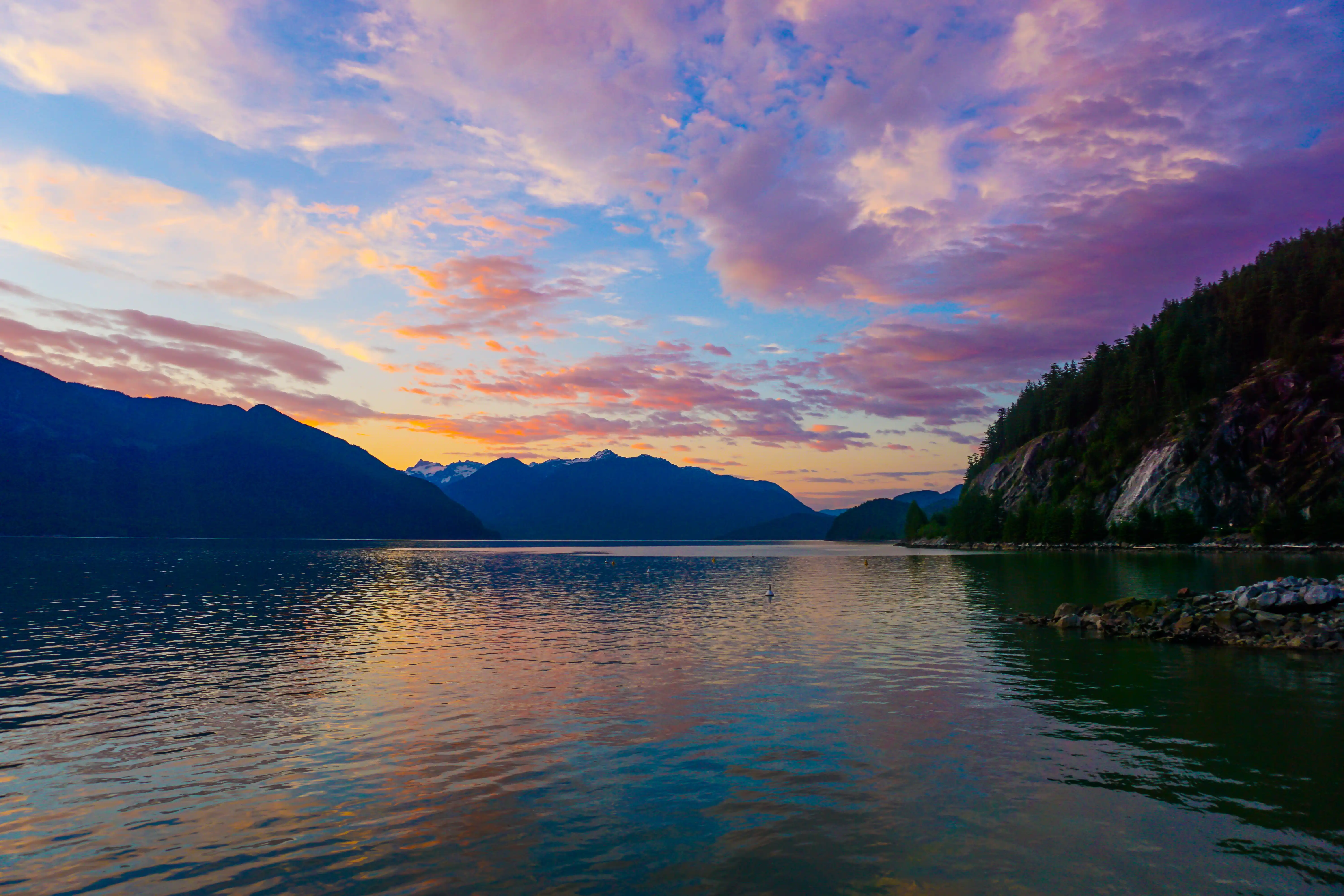 Sunset colors reflected on a calm lake surrounded by dark mountains.