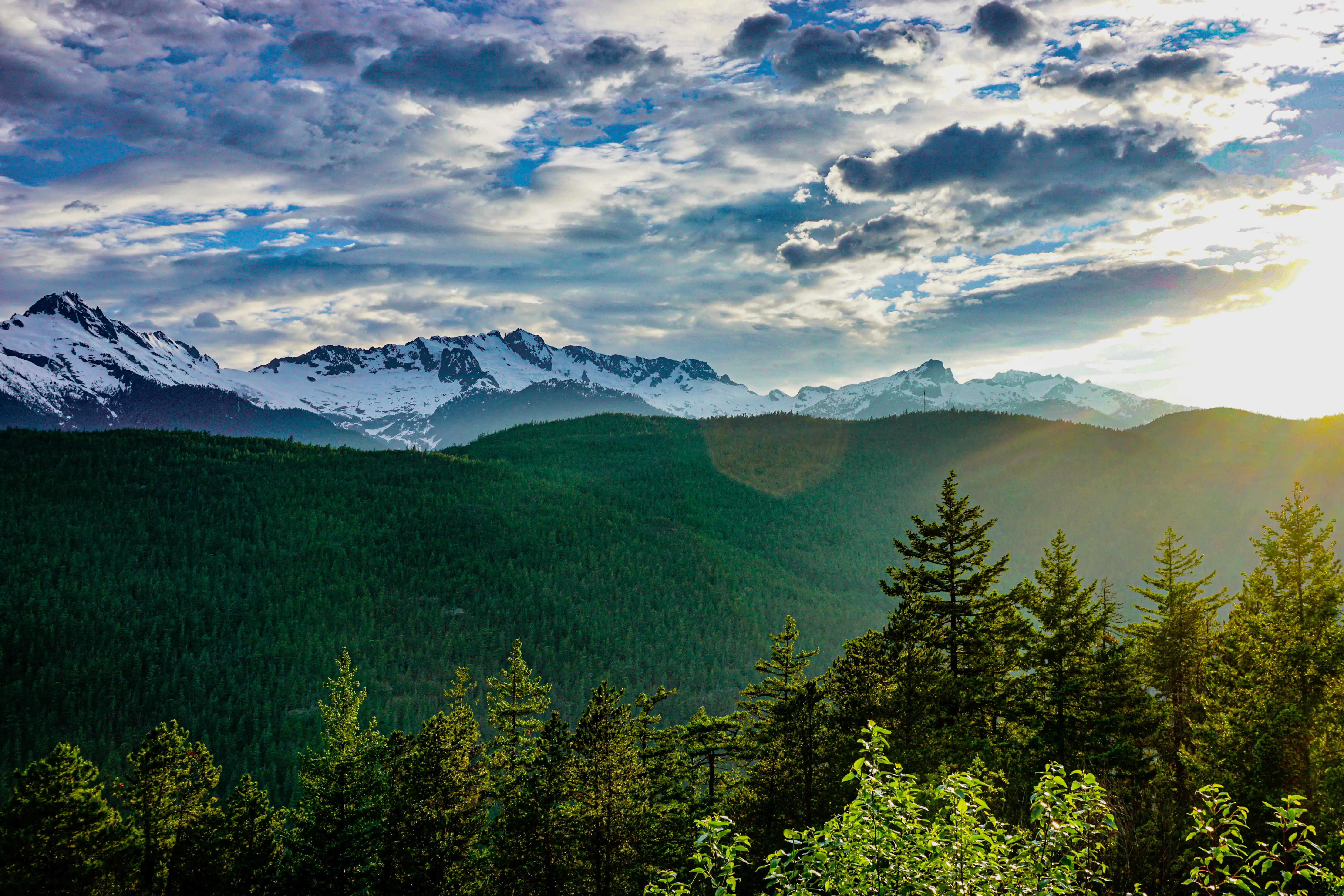 Green mountain ridge beneath bright clouds and distant snow-covered peaks.