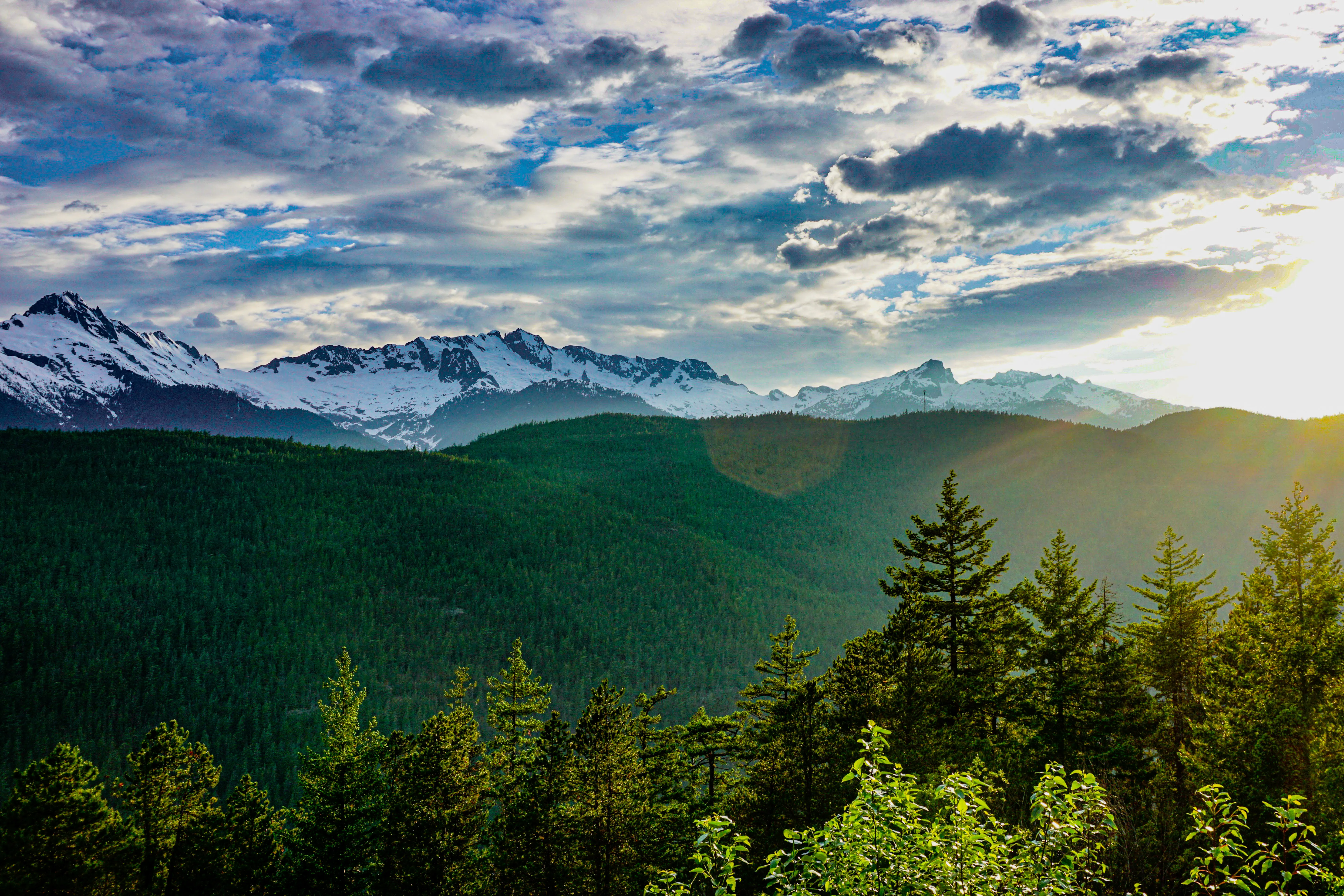 Green mountain ridge beneath bright clouds and distant snow-covered peaks.
